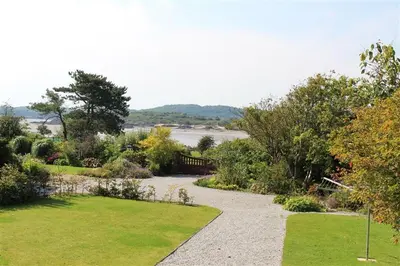 a walkway through a garden with a view of the water at Seabank Cottage in Rockcliffe