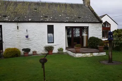 a white house with a porch and a yard at Ernambrie Cottage in Castle Douglas