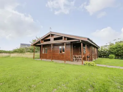 a wooden cabin in a field with a grass field at Curlew Lodge in Dumfries
