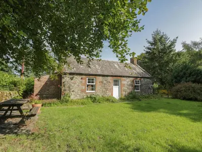 an old stone house with a picnic table in the yard at Little Dunbar Cottage in Dumfries
