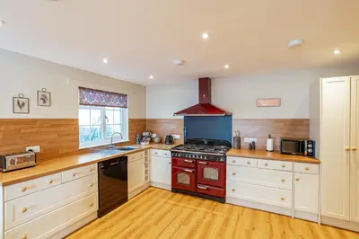 a kitchen with white cabinets and a red stove top oven at Sparrowhawk Cottage with Hot Tub in Newton Stewart