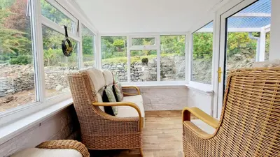 a screened in porch with wicker chairs and windows at Nordlys Cottage in Newton Stewart