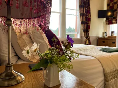 a bedroom with a bed with a vase of flowers on a table at Maple Bank Country Guest House in Keswick