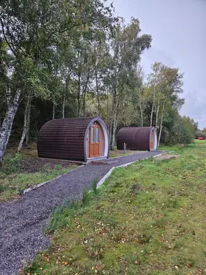 two small buildings in a field with trees at Broom Leisure Camping Pods in Annan