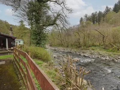 a river with a wooden fence next to a house at Chestnut Timber Lodge in Keswick