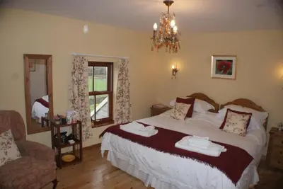 a bedroom with a bed and a chair and a mirror at Knockaloe Beg Farm in Patrick