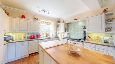 a kitchen with white cabinets and a wooden counter top at Airds of Kells House in Castle Douglas