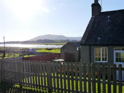 a fence in front of a house with a lake at Branta Cottage in Dumfries