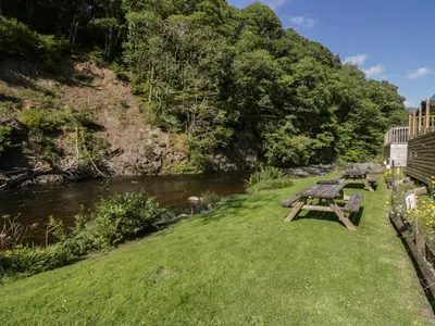 a picnic table on the grass next to a river at Garden Cottage No 1 in Keswick