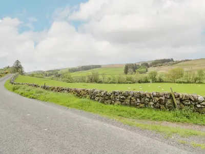 a road with a stone wall next to a field at High Auchenbrack in Thornhill