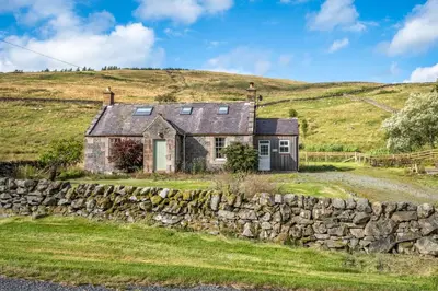 a stone house on a hill with a stone wall at Prince's Cottage in Thornhill