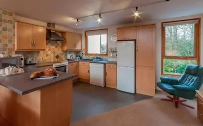 a kitchen with wooden cabinets and a blue chair at Keswick Bridge 17, within walking distance of Keswick town centre, strictly no pets in Keswick
