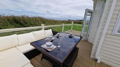 a table with wine glasses on a balcony at Seaside Heaven - Southerness Caravan Rental in Mainsriddle