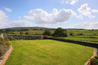 a large yard with a stone wall and green grass at Teapot Cottage in Newton Stewart