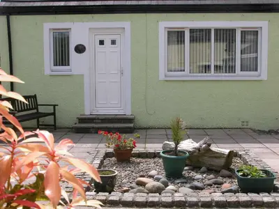 a green house with a white door and some plants at Ash Cottage in Stranraer