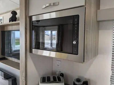 a kitchen with a microwave above a stove at Beautiful Pet Friendly Southerness Caravan With Sea View & Decking Area in Mainsriddle