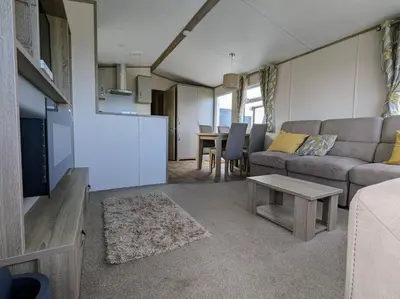 a living room with a couch and a table at Beautiful Pet Friendly Southerness Caravan With Sea View & Decking Area in Mainsriddle