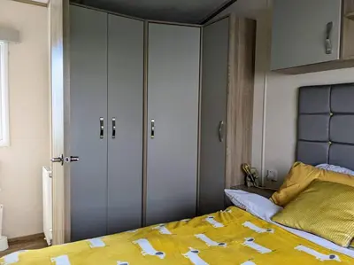 a bedroom with a bed and two closets with yellow sheets at Beautiful Pet Friendly Southerness Caravan With Sea View & Decking Area in Mainsriddle
