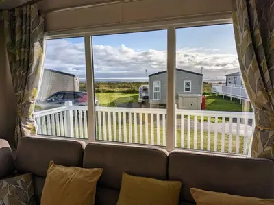 a couch sitting in front of a large window at Beautiful Pet Friendly Southerness Caravan With Sea View & Decking Area in Mainsriddle