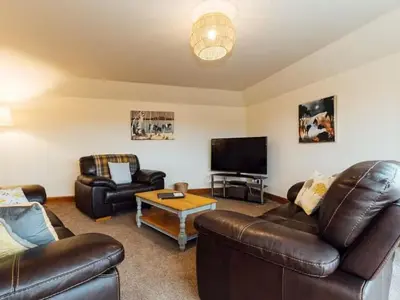 a living room with leather furniture and a flat screen tv at Middle Byre at Clauchan Holiday Cottages in Gatehouse of Fleet