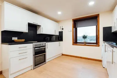a kitchen with white cabinets and a window at The Barn @ Clauchan holiday Cottages in Gatehouse of Fleet