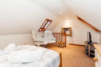 a bedroom with a bed and two chairs and a television at The Dairy Bothy at Clauchan Holiday Cottages in Gatehouse of Fleet