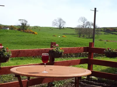 a table with a glass of wine sitting on a fence at The Dairy Bothy at Clauchan Holiday Cottages in Gatehouse of Fleet