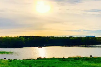 a boat on a lake with the sun in the sky at Bridgend Cottage, Auchencairn, Castle Douglas in Auchencairn