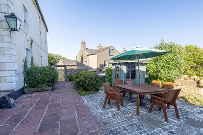 a patio with a wooden table and chairs and an umbrella at Historic St Bees Farmhouse Hot Tub Games Summer Gatherings in St Bees