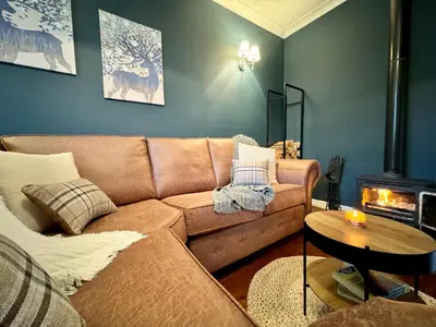 a living room with a brown couch and a fireplace at Chestnut Cottage in Dalmellington