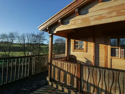 a wooden cabin with a wooden railing on a deck at Ballinorig Lodge in Cleator Moor