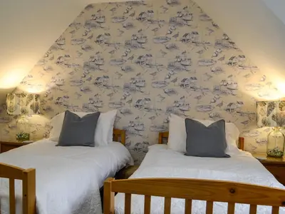 two beds in a bedroom with blue and white wallpaper at Clachries Cottage in Boreland of Colvend