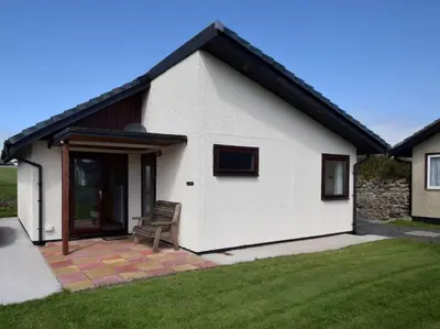 a white house with a chair in a yard at 2 Bed in Isle of Whithorn 77880 in Isle of Whithorn