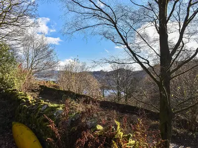 a tree and a fence with a view of the mountains at Tarn Cottage in Grasmere