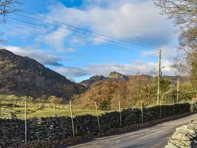 a road with a stone wall and mountains in the background at Lingmoor View in Ambleside