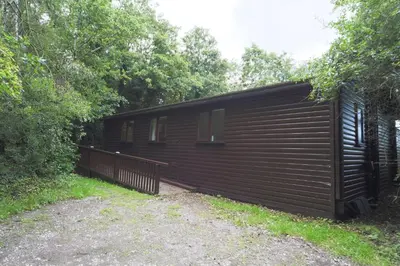 a large wooden building with a fence next to trees at Egret Lodge with Hot-tub in Carlisle