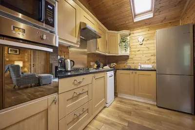 a kitchen with wooden cabinets and a stainless steel refrigerator at Fieldfare Lodge with Hot-tub in Carlisle