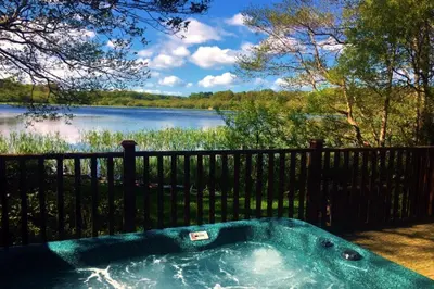 a hot tub in front of a fence next to a lake at Gadwall Lodge with Hot-tub in Carlisle