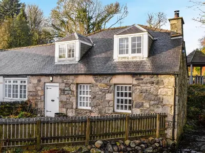 an old stone house with a wooden fence at The Smithy in New Galloway