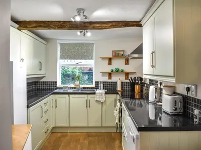 a kitchen with white cabinets and black counter tops at Daffodil Cottage in Cockermouth