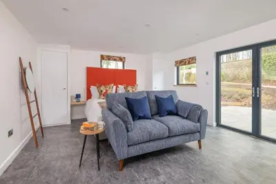 a living room with a gray couch and windows at Shepherds Retreat Hutton John in a walled garden in a rural setting only 10 minutes for Lake Ullswater in Penruddock