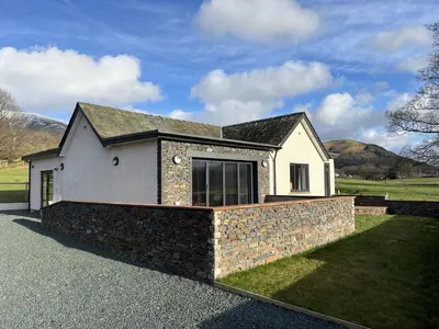 a white house with a stone wall at Langrigg Cottage HOT TUB HIRE AVAILABLE in Portinscale