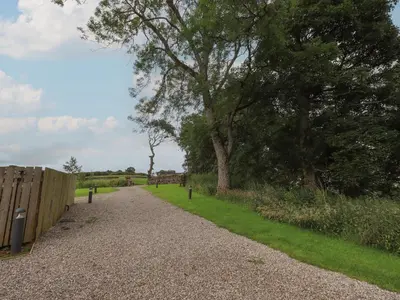 a gravel road with a fence and trees at Herdwick Cabin in Penrith
