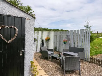 a fence with a black door and chairs and a table at High Wreah Bolt Hole in Whitehaven