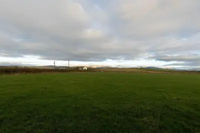a field of green grass with a house in the background at Escape to our Cosy Cottage with Log Burner in Drigg, Lake District in Drigg