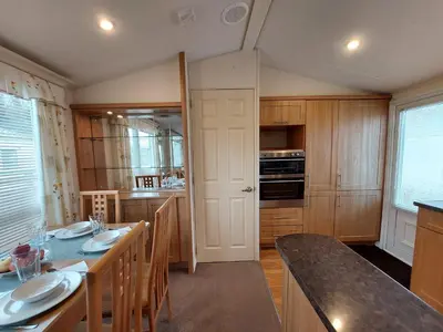 a kitchen with wooden cabinets and a table with chairs at Winnie - Caravan mit Meerblick in Drummore