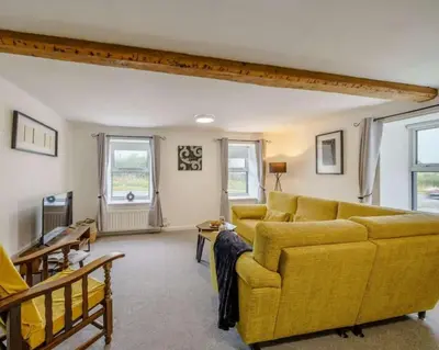 a living room with a yellow couch and two windows at Barncroft: Dogs welcome, dog care services offered in Cockermouth