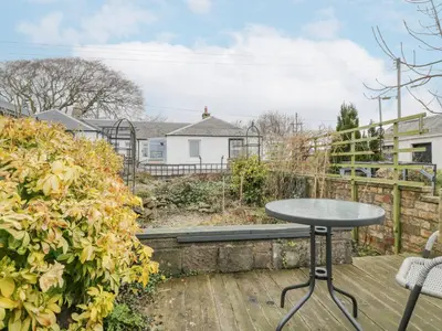a patio with a table and chairs on a wooden deck at Rosalin Cottage in Irvine