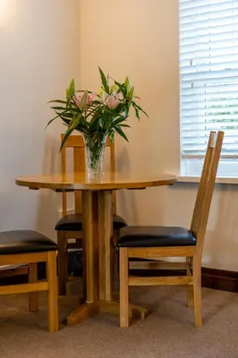 a vase of flowers on a wooden table with chairs at Acorn Apartment 1 in Keswick