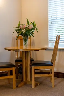 a vase of flowers on a wooden table with chairs at Acorn Apartment 1 in Keswick